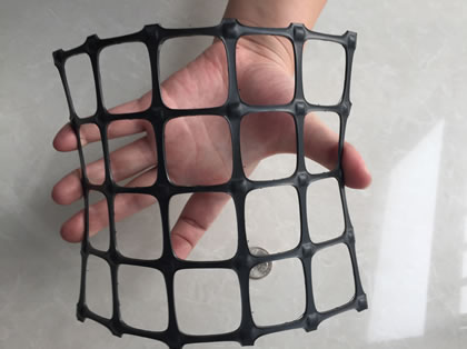 A hand is bending a piece of black biaxial geogrid.