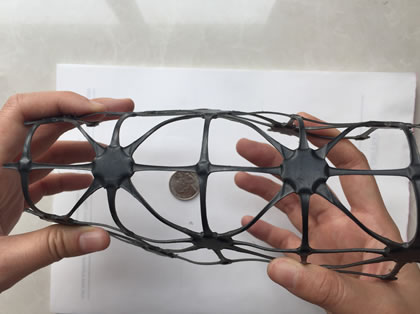 Two hands are bending a piece of trixial geogrid.