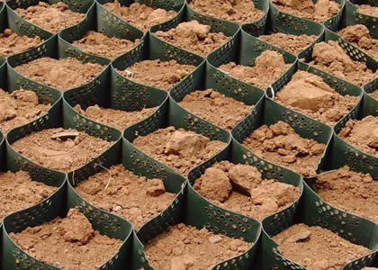 A piece of green perforated geocell is filled with soft soil.