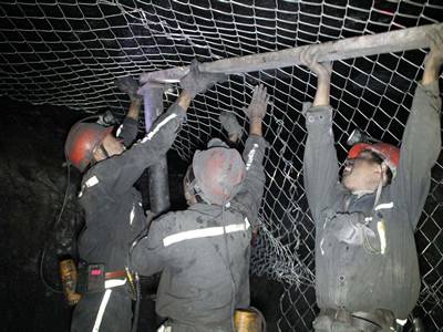 Four workers are installing the chain link meshes onto the roadway roof.